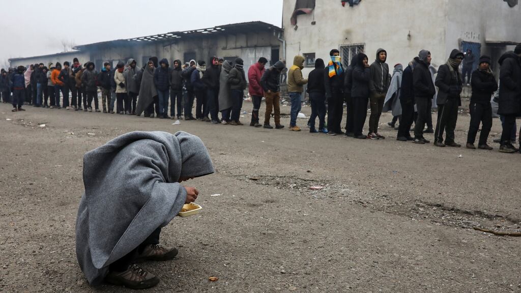A migrant eats as others stand in line to receive free food outside a derelict customs warehouse in Belgrade, Serbia. Photograph: Marko Djurica/Reuters