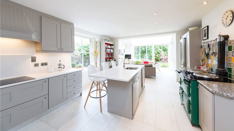 The kitchen, with a centre island and stone worktops, has a green Aga with a colourful Fired Earth splashback
