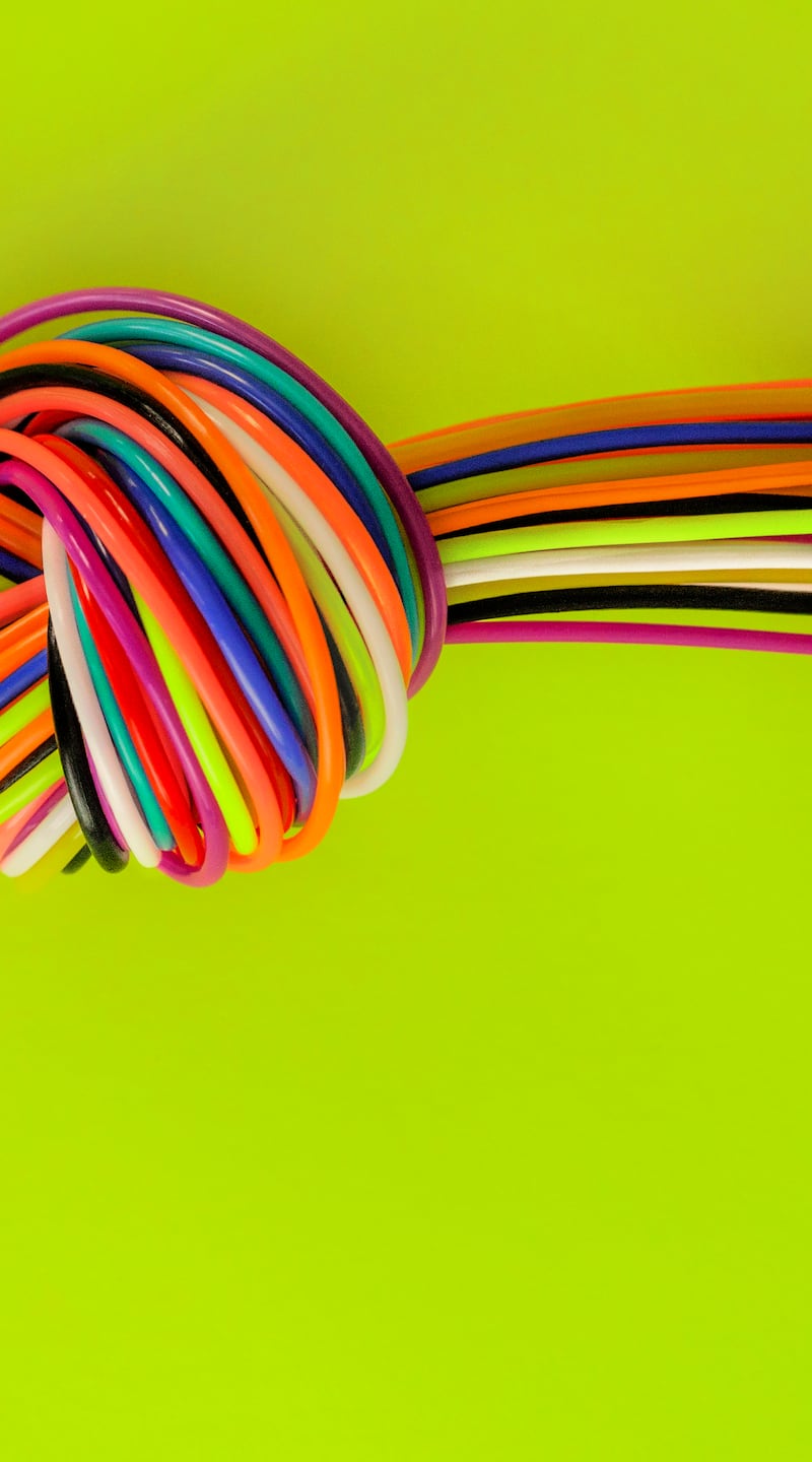 Horizontal  photo of a KNOT made up of multi-colored PLASTIC strands. Knot is displaced above center on the page, and laying on a NEON yellow green background with copy space. Knots can be a metaphor for such things as emotional stress, or stalemate in negotiations or plastic choking the planet. There is copy space in lower half of image.