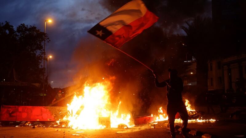 A demonstrators waves a Chilean flag in front of burning debris in Santiago on Friday. Photograph: Fernando Bizerra jr/EPA