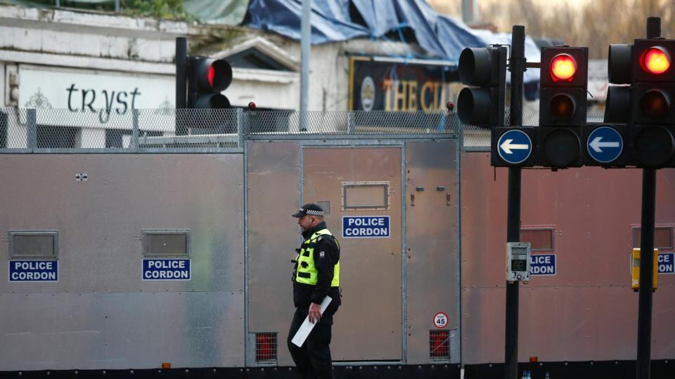 An officer walks past a police cordon set up around the site of the helicopter crash. Part of the aircraft are covered by the tarpaulin behind. Photograph: Andrew Winning/Reuters