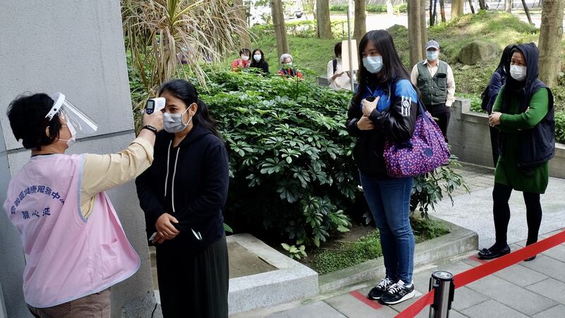 A masked local resident has her temperature checked as people line up to buy face masks from vending machines at a health centre in Taipei. File photograph: Getty