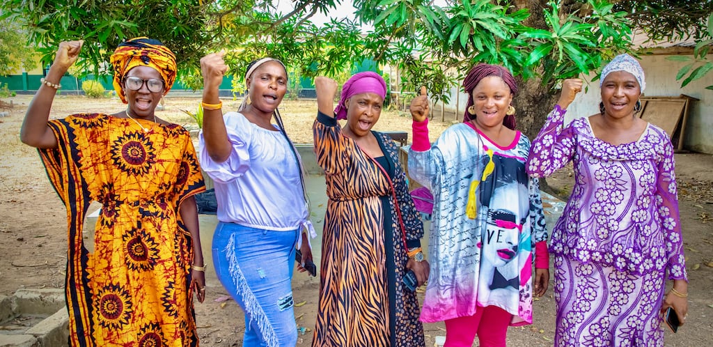 Women raise their arms in a symbol of unity during a Goila women's group meeting in Magbankani, Sierra Leone.