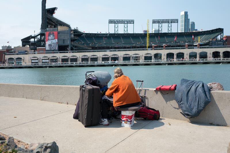 A homeless man stares across McCovey Cove towards ATT Park, the baseball stadium of the San Francisco Giants, in the China Basin neighborhood of San Francisco, California. Photo by Smith Collection/Gado/Getty Images.