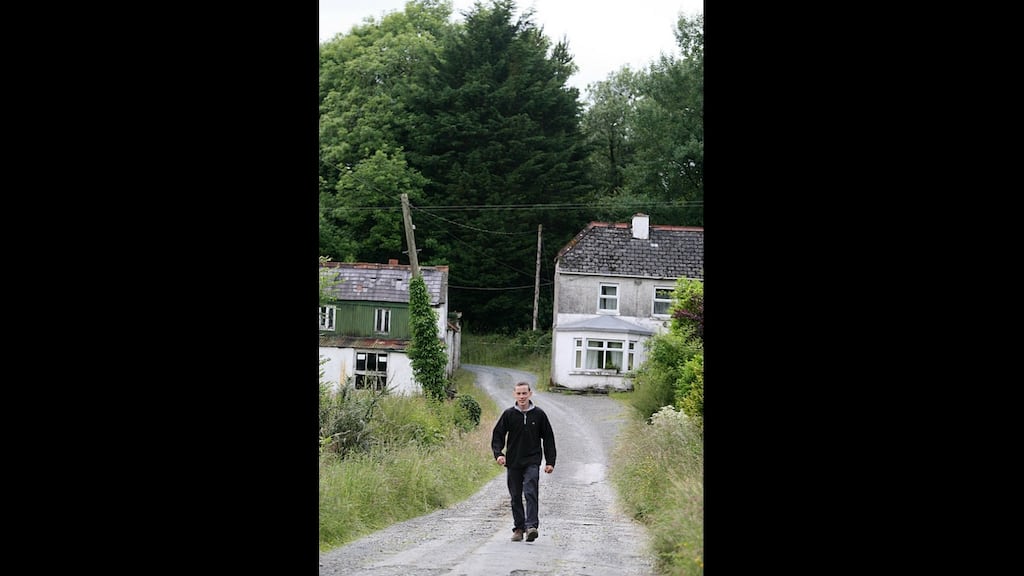 Adrian Kelly from Cloone, Co Leitrim, passing a former shop (left) and a house which are both surrounded by forestry. “How can you live with trees coming up to your door?” Photograph: Brian Farrell