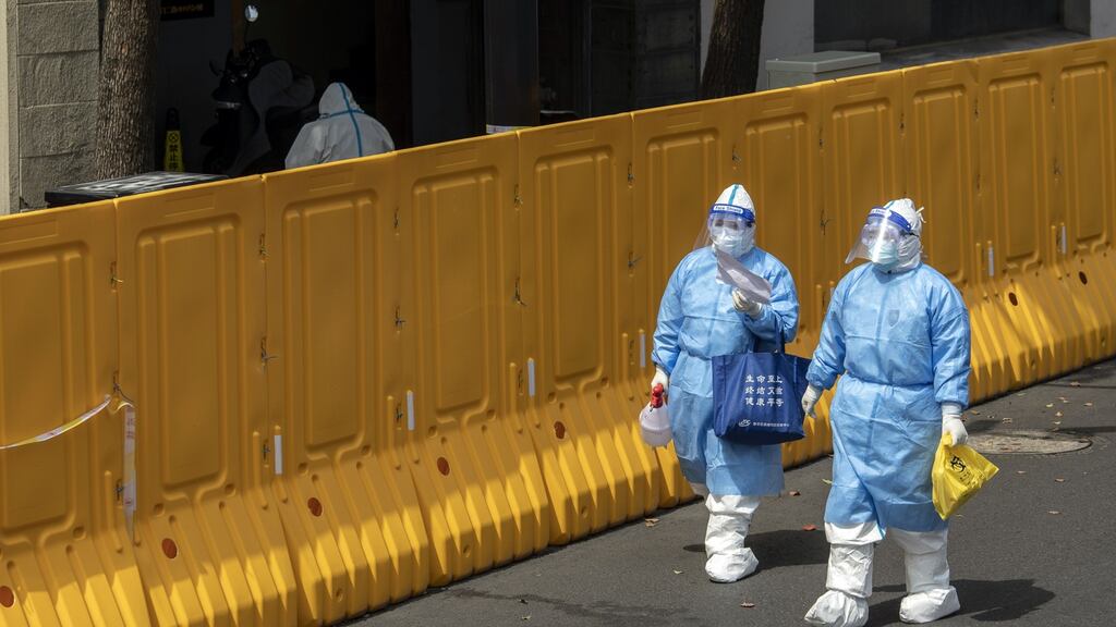 Workers wearing personal protective equipment (PPE) walk past a perimeter wall of a neighborhood under lockdown due to Covid-19 in Shanghai, China, on Wednesday. Photograph: Qilai Shen/Bloomberg