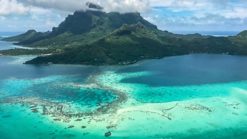 An aerial view of Bora Bora island in French Polynesia over a pristine turquoise lagoon and under the volcanic Mount Otemanu
