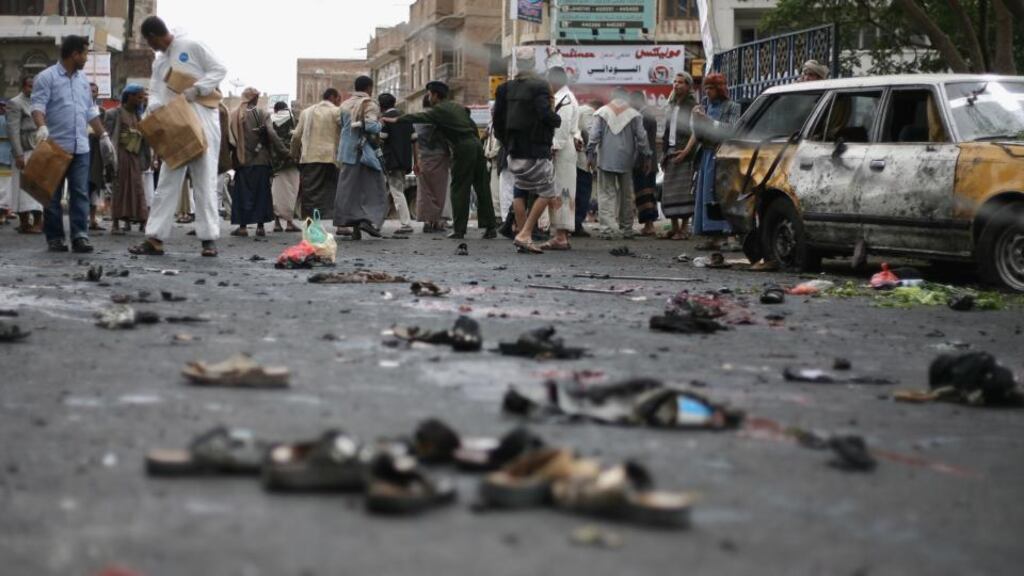 People gather at the site of a suicide bombing as Yemeni security officials collect debris in Sanaa, yesterday. Photograph: AP