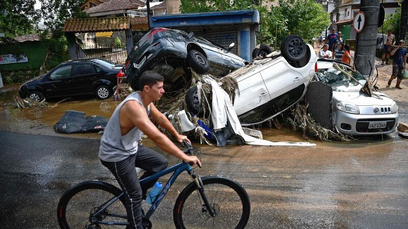 A man rides his bicycle past cars destroyed by a flash flood in Petropolis, Brazil. Photograph: Carl de Souza/AFP via Getty Images