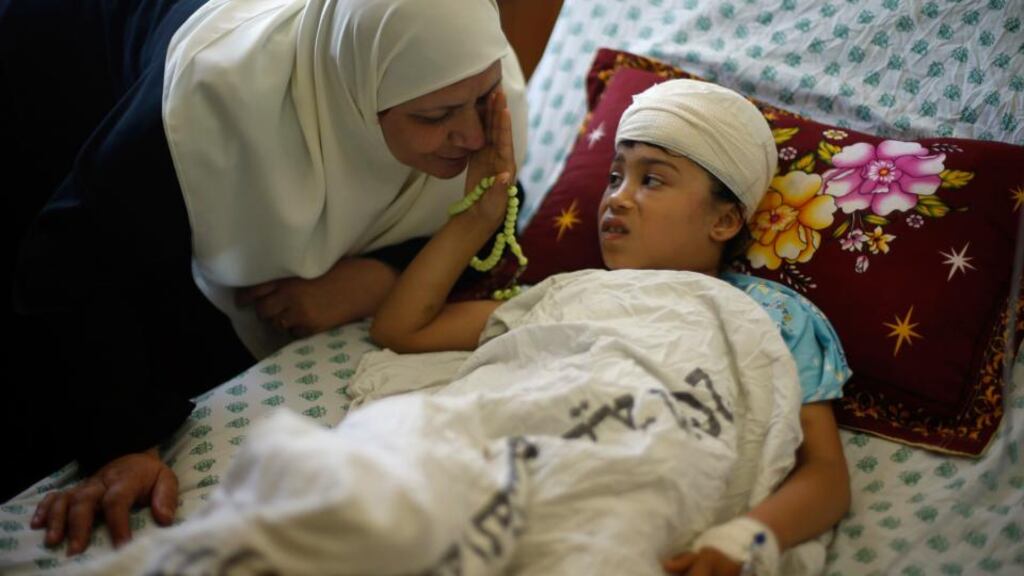 Nine-year-old Palestinian Maryam Al-Masri, whom hospital officials said was wounded in an Israeli air strike, listens to her grandmother as she lies on a bed while receiving treatment at a hospital in Gaza City yesterday. Photograph: Reuters/Mohammed Salem
