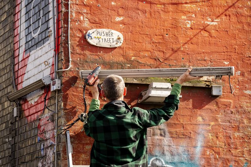 A resident of the Christiania neighbourhood uninstalls a neon lamp on a building at Pusher Street, in Copenhagen, Denmark, in 2024. Photograph: Ida Marie Odgaard/Ritzau Scanpix/AFP via Getty Images
