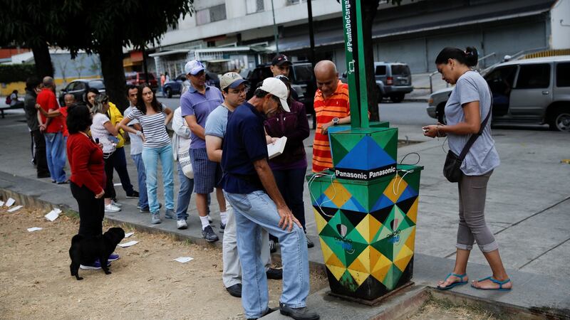 People queue to charge their phones with a solar panel at a public square in Caracas as mass power cuts continue. Photograph: Carlos Garcia Rawlins/Reuters