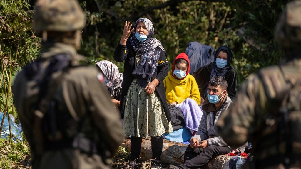 A woman talks to a Polish border guard as migrants believed to be from Afghanistan sit on the ground in the small village of Usnarz Gorny, northeastern Poland, located close to the border with Belarus. Photograph: Wojtek Radwanski/AFP via Getty Images