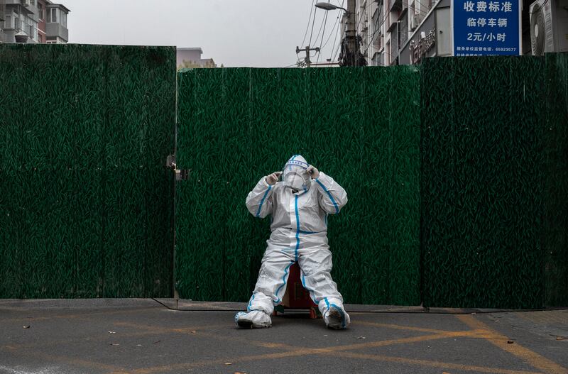An epidemic control worker in Beijing adjusts his face shield as he wears a protective suit while guarding in front of a barrier fence in an area under lockdown. Photograph: Kevin Frayer/Getty Images