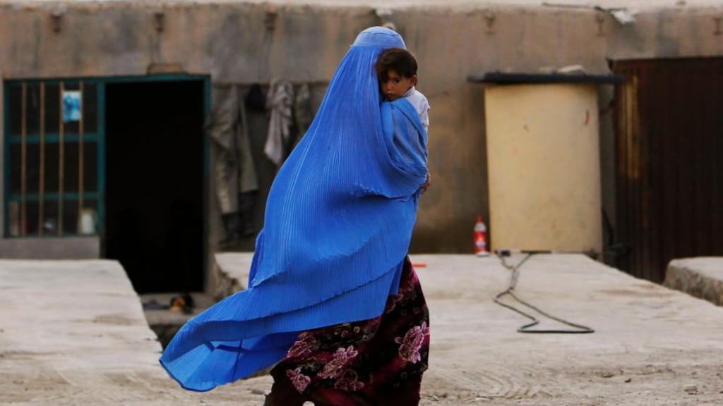 An Afghan woman wearing a burqa carries a child  along a street on the outskirts of Kabul. Photograph: Omar Sobhani/Reuters