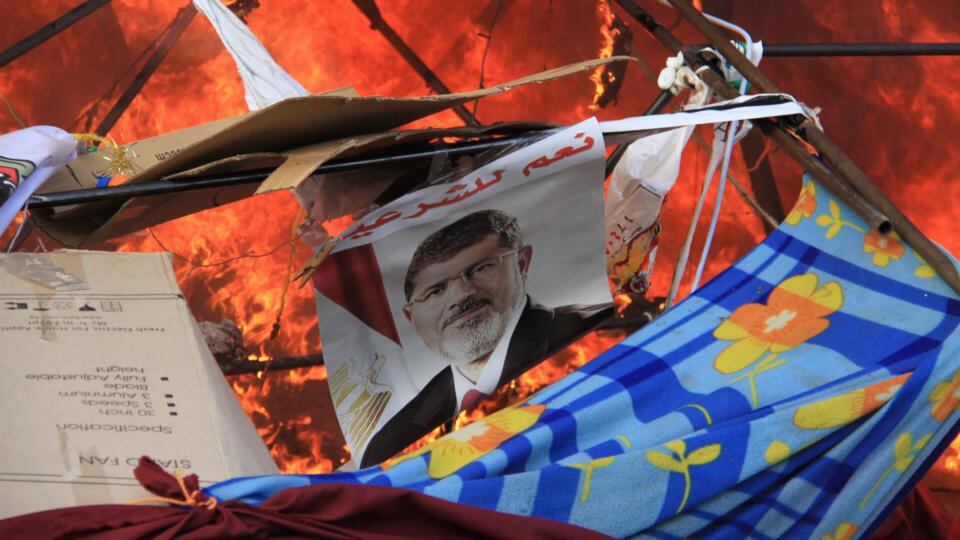 A poster of deposed Egyptian president Mohamed Morsi reads “Yes to legitimacy” amid flames as riot police clear Rabaa Adawiya square   in Cairo of members of the Muslim Brotherhood and Morsi supporters today. Photograph: Reuters