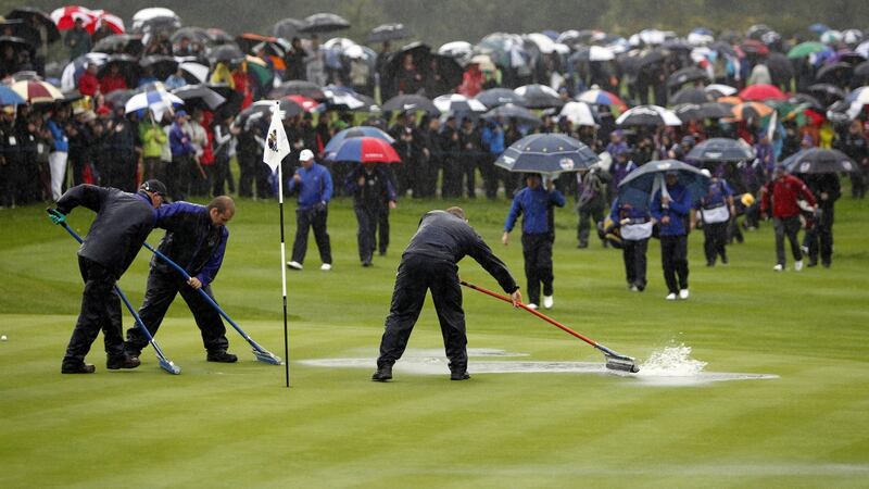 Groundstaff clear standing rain water from the third green as the players approach. Photo: Peter Muhly/AFP via Getty Images