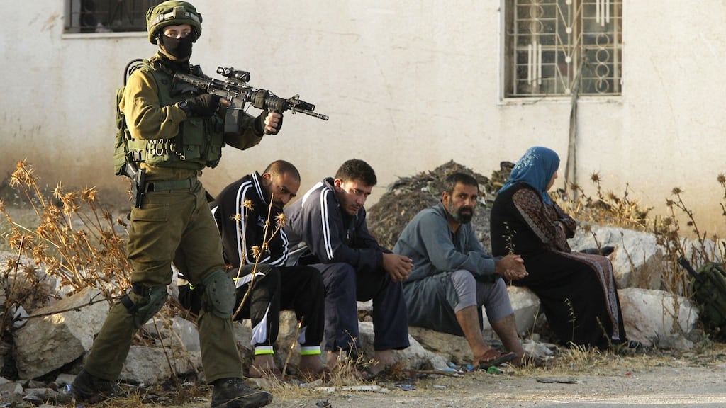 An Israeli soldier keeps watch over  Palestinians  after the army entered the village of Yatta in the occupied West Bank on  in search for clues leading to an attack the previous night in the Israeli city of Tel Aviv. Photograph: Hazem Bader/ AFP/Getty Images