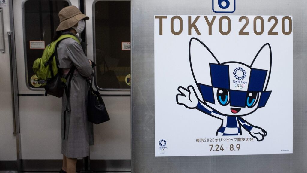 A passenger wearing a face mask stands next to a poster of Tokyo 2020 Olympic mascot Miraitowa on a train in Tokyo. Photo: Philip Fong/AFP via Getty Images
