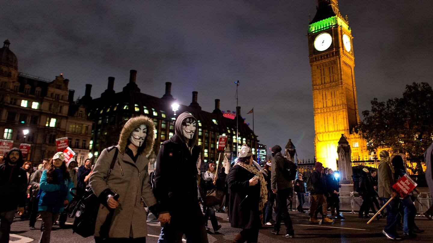 Masked protesters pass in front of the Houses of Parliament during the Million Mask March. Photograph: Photograph: Getty