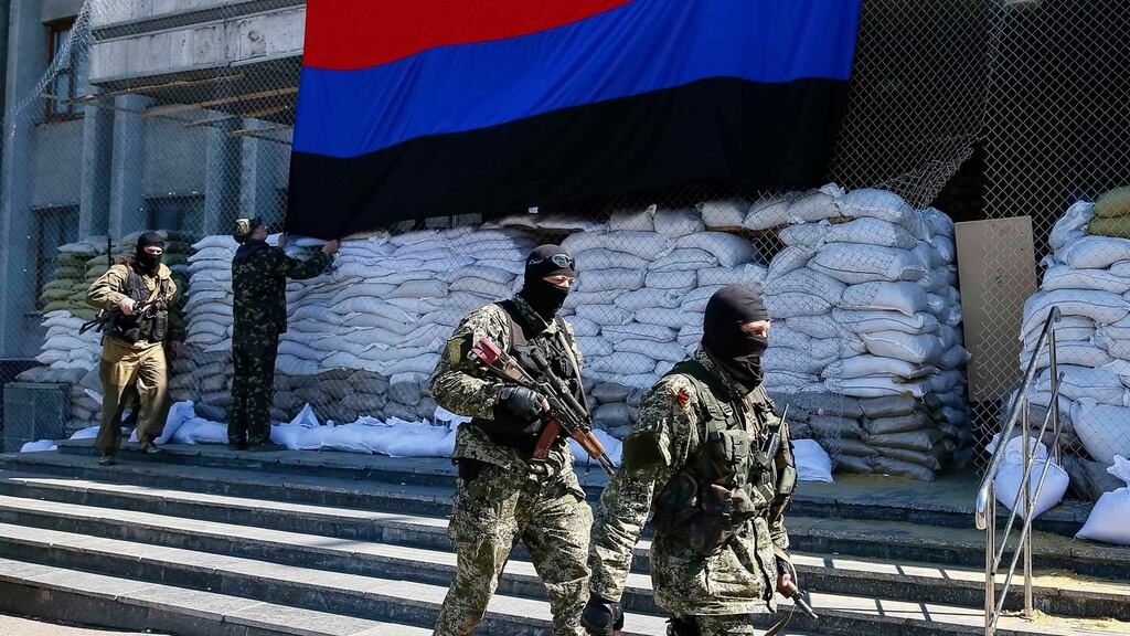 Pro-Russian armed men walk past activists hanging up a ‘Donetsk Republic’ flag outside the mayor’s office in Slaviansk today. Photograph: Gleb Garanich/Reuters
