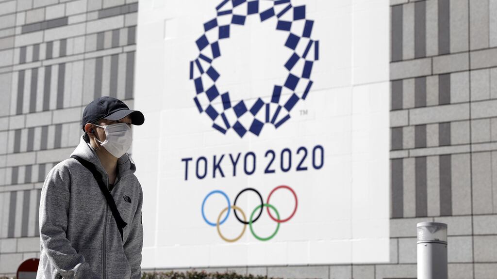 A pedestrian wearing a protective face mask walks past a banner featuring the emblem for the Tokyo 2020 Olympic Games. Photo: Kiyoshi Ota/Bloomberg