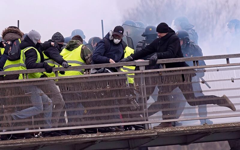 Former French boxing champion, Christophe Dettinger (right in black hat), kicks a French gendarme on the ground during violent clashes on a pedestrian footbridge during a  ‘gilets juanes’ demonstration in Paris on January 5th Photograph:  Ian Langsdon/EPA