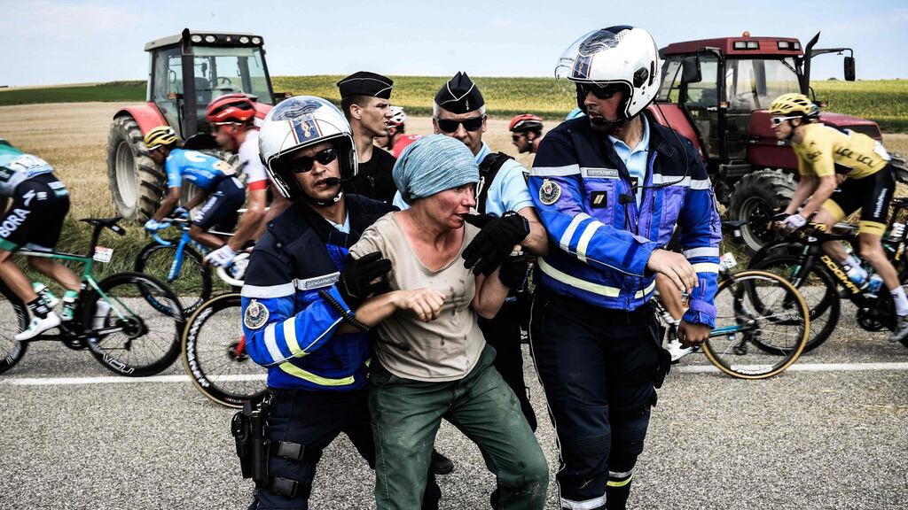 Gendarmes detain a protester as  Geraint Thomas, wearing the overall leader’s yellow jersey, and the pack ride behind. The race was halted for several minutes on   after tear gas was used as protesting farmers attempted to block the route. Photograph: Getty Images