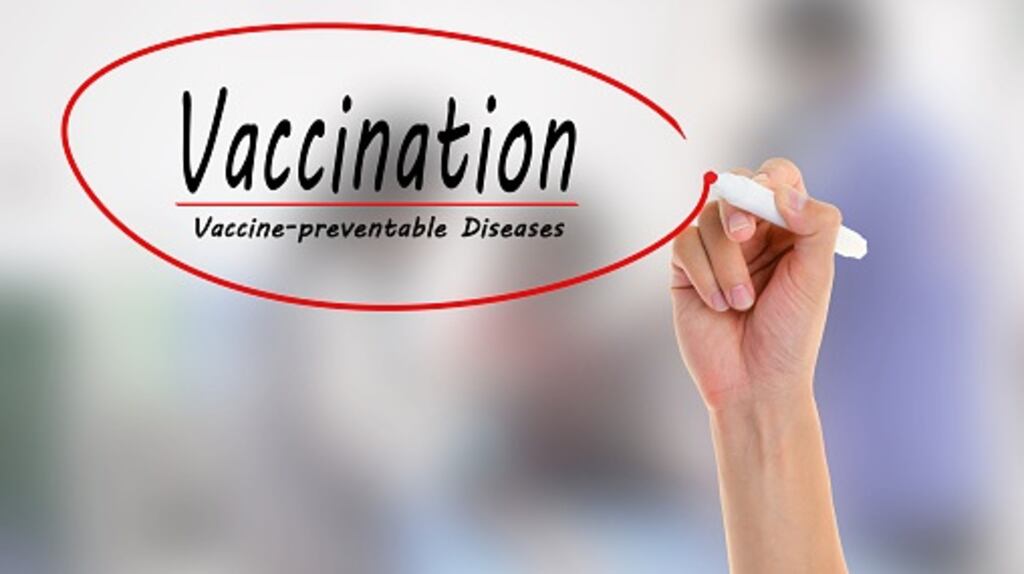 Doctor hand writing Vaccination on blurred of vaccine injection.