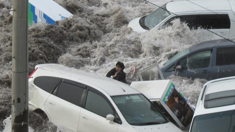 A reporter for local newspaper Iwate Tokai Shimbun, is caught up in the tsunami. He managed to survive the tsunami by grabbing a dangling rope and climbing onto a coal heap. Photograph: Kyodo News Stills via Getty Images