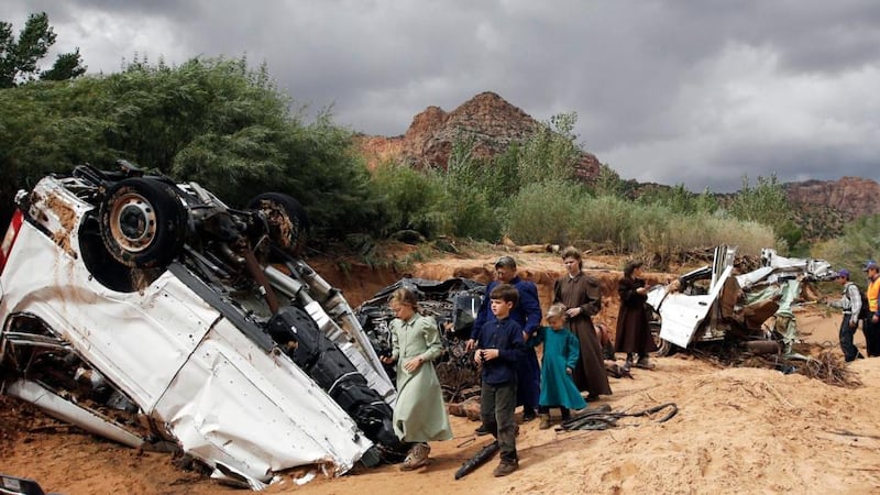 People walk pass a severely damaged vehicle swept away by a surge of water during a flood in Hildale, Utah. The floodwater swept away a number of vehicles in the Utah-Arizona border town, killing at least 15. Photograph: AP