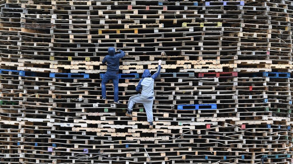 Two youths climbing a huge Eleventh Night bonfire in east Belfast