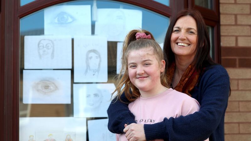 Ellen Cahill, a community group organiser in the Ballymurphy estate, Belfast, with her daughter Aoibhe and some of the pictures the local children have drawn to place in the front windows of their houses to brighten up their neighbourhood. Photograph:  Stephen Davison