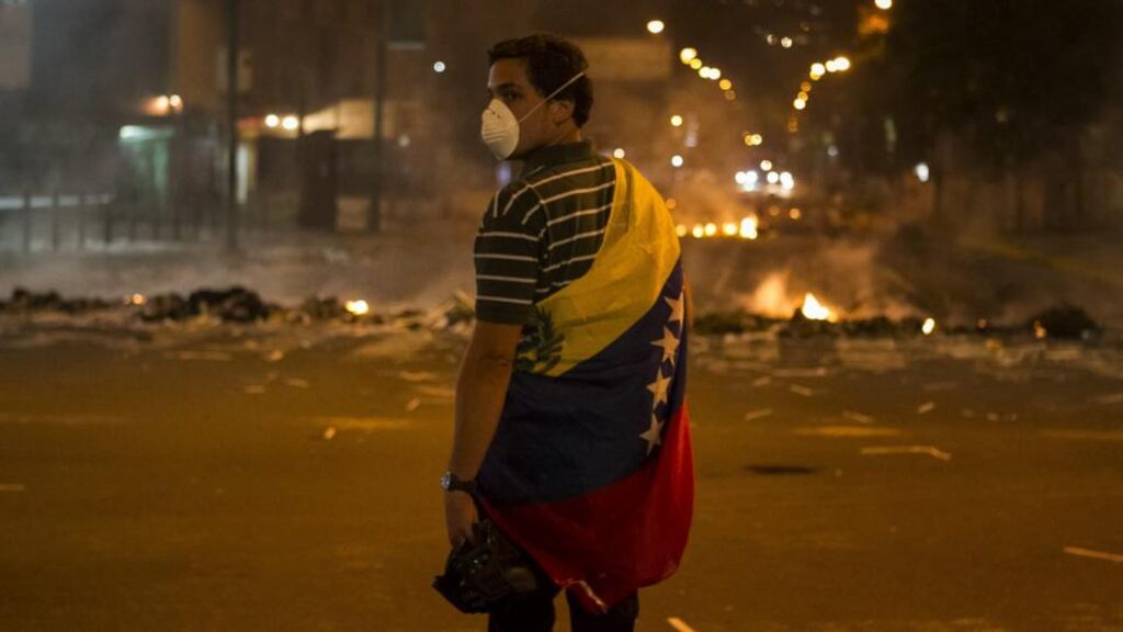 A man wrapped in the Venezuelan flag stands close to a fire at a barricade during a protest against Venezuelan government in Altamira, Caracas. Photograph: Miguel Gutierrez/EPA.