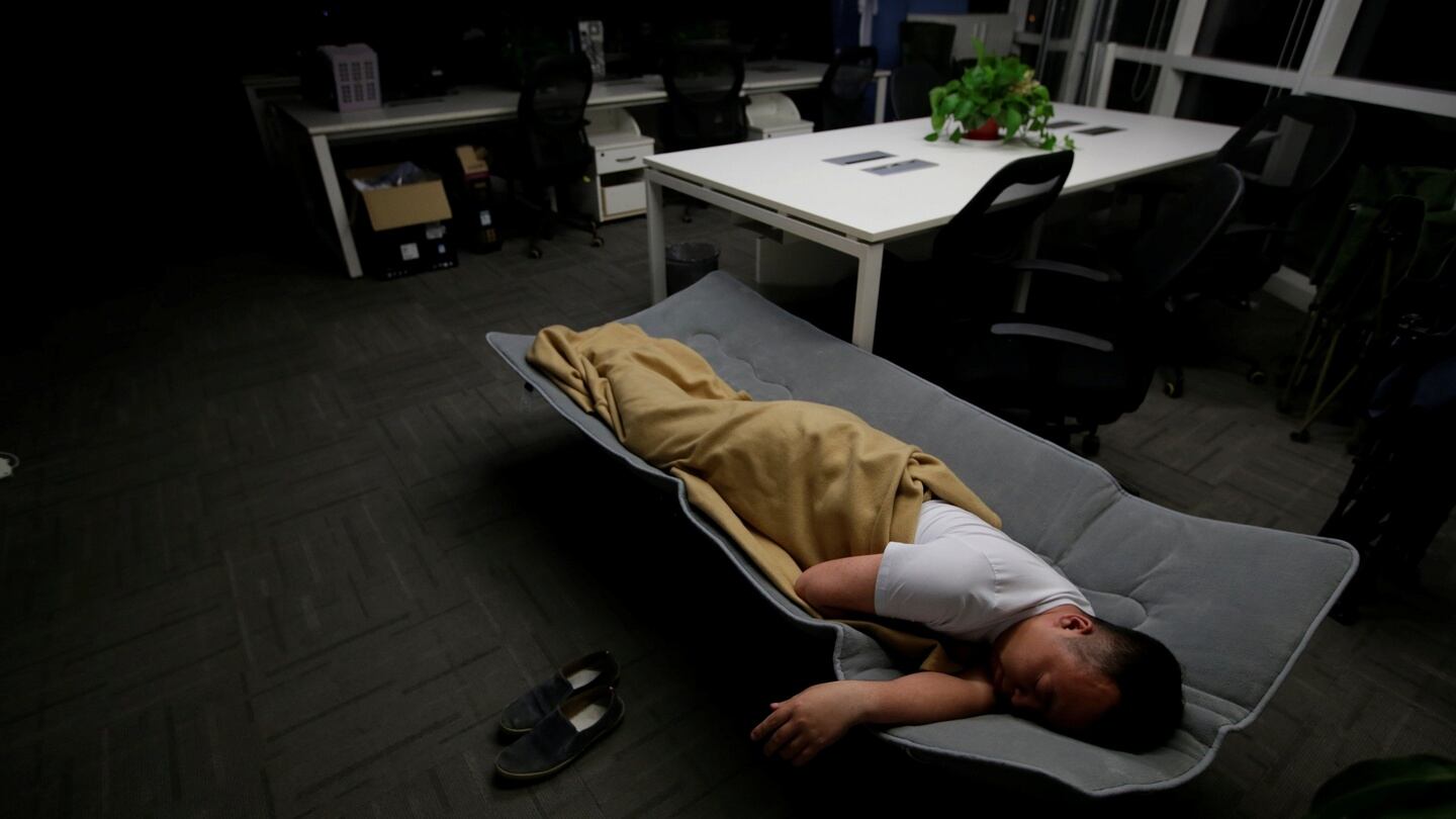 Ma Zhenguo, a system engineer at RenRen Credit Management sleeps on a camp bed at the office after finishing work in the early mornin. Office workers sleeping on the job is a common sight in China. Photograph: Jason Lee