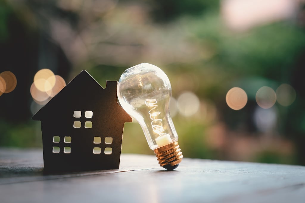 A light bulb rests against a wooden model of a house on a table