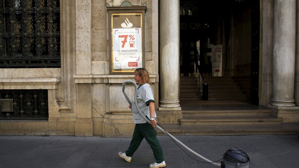 A cleaner pulls a vacuum cleaner as she walks past a Santander Bank branch in the Andalusian capital of Seville, southern Spain