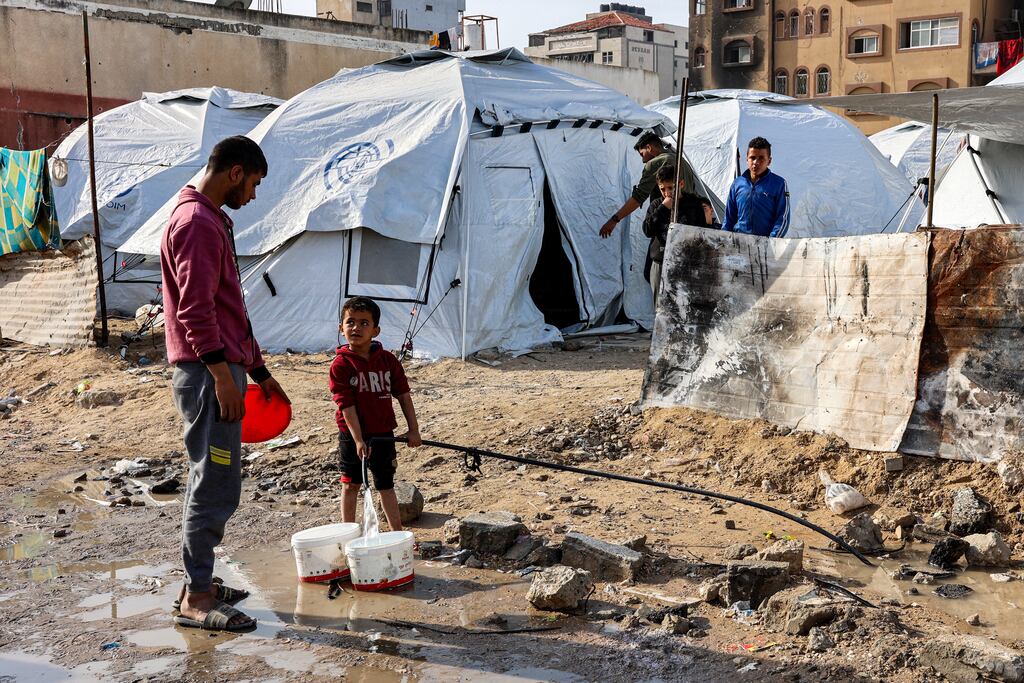 A youth speaks to a boy filling up buckets with water from a hose near tents at a shelter for displaced Palestinians in Gaza City on December 11th amid the continuing war in the Palestinian territory between Israel and Hamas. Photograph: Omar Al-Qattaa/AFP via Getty Images