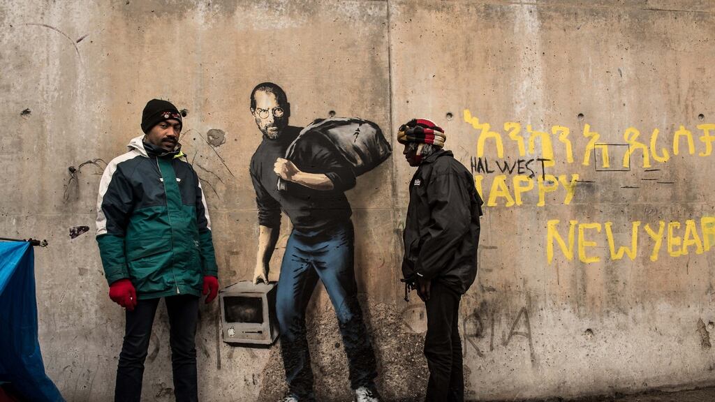 Two men stand next to  graffiti by elusive British artist Banksy representing Steve Jobs, founder and late chief executive  of Apple, at the migrant camp known as the “Jungle” in Calais, northern France,  December 12th, 2015.  Photograph: Philippe Huguen/AFP/Getty Images