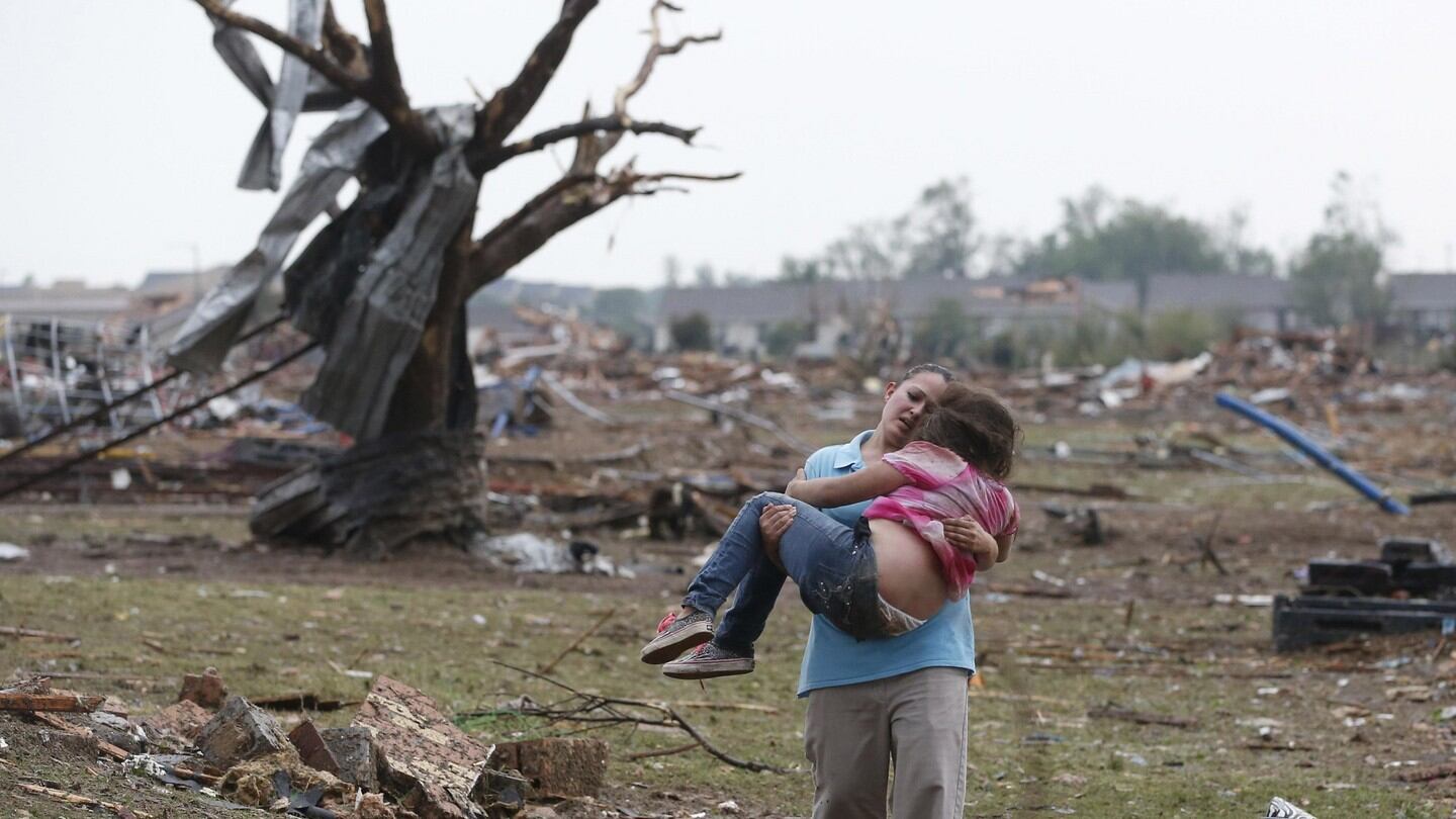 A woman carries her child through a field near the collapsed Plaza Towers Elementary School in Moore, Oklahoma.