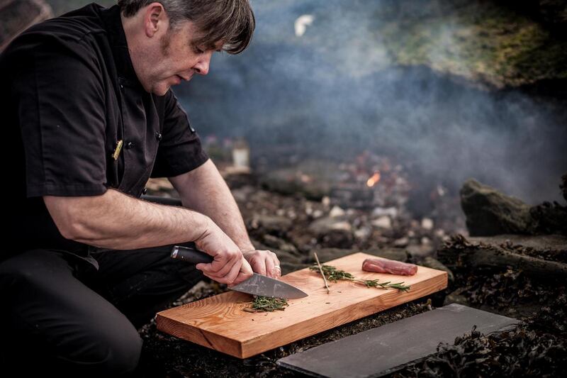 William McElhinney preparing food in an outdoor firepit