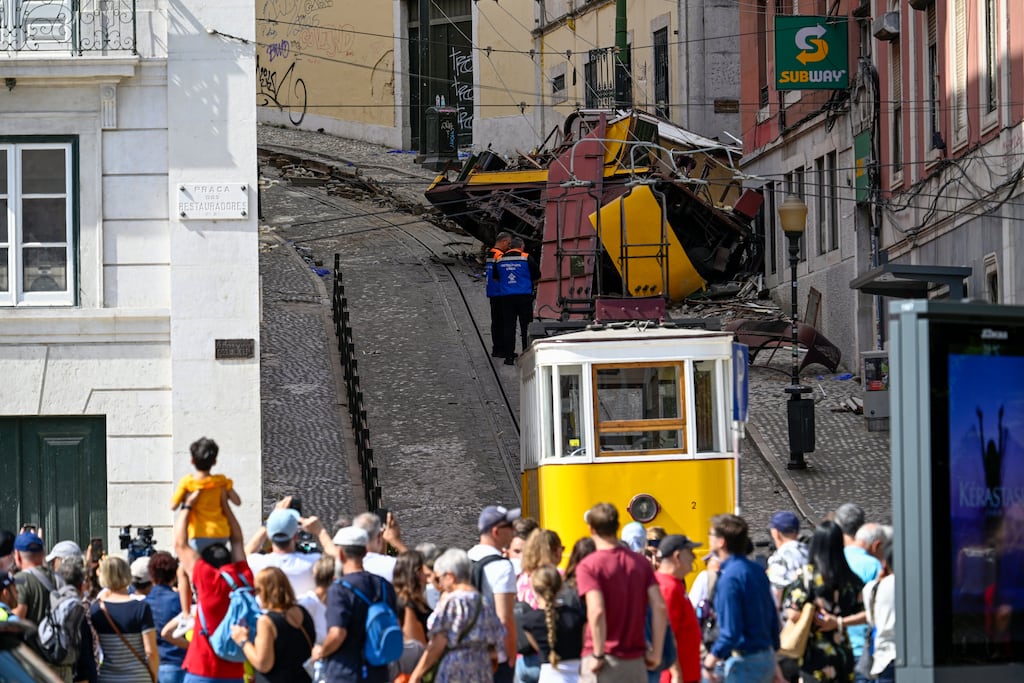 Onlookers stand behind a police line as officials inspect the area surrounding a wrecked Glória Funicular streetcar in Lisbon. Photograph: Horacio Villalobos/Getty Images