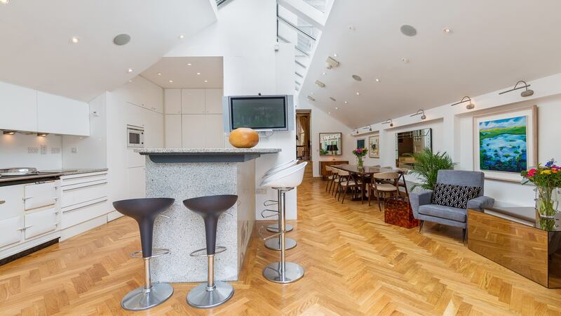 On one side of the room divider is a sleek fitted kitchen; on the other is a dining space furnished with a long dining table