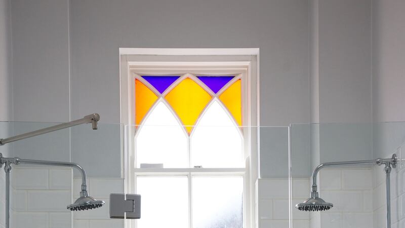The step-up shower stall is tiled in classic metro ceramics and frames a coloured glass period feature window. Photograph: Emily Quinn