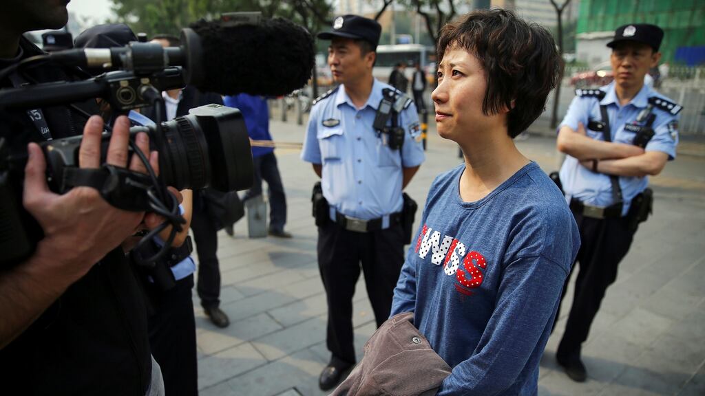 Policemen stand behind Lin Ru, the wife of civil rights lawyer Xia Lin, as she talks to media near a Beijing court on Thursday after her husband was sentenced to 12 years in prison on fraud charges. Photograph: Damir Sagolj/Reuters