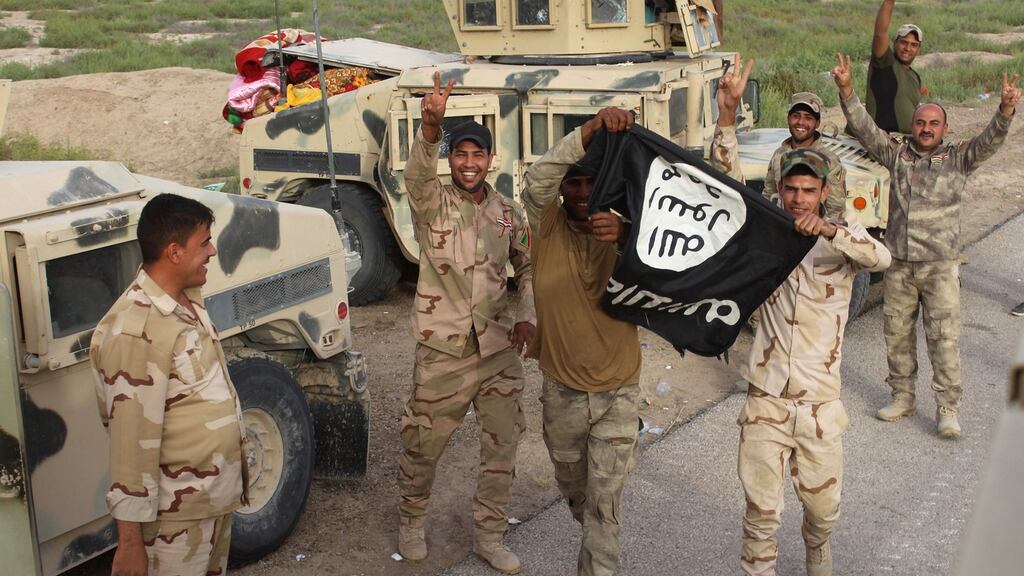 Fighters from Iraqi pro-government forces hold up an Islamic State flag and flash the V-sign during a military operation against Isis near Amriyat al-Falluja, 30km south of the besieged city of Fallujah. Photograph: Moadh al-Dulaimi/AFP/Getty Images