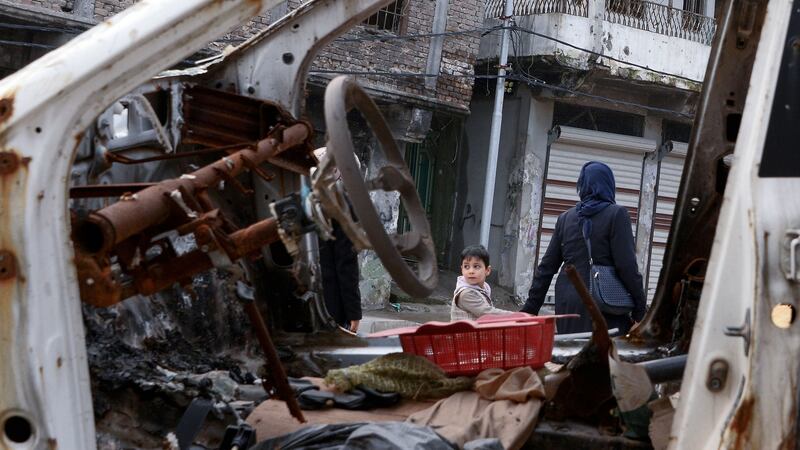An Iraqi boy holding a woman’s hand walk past a destroyed car in the old town area of Souk al-Shaarin, in Mosul. Photograph: Getty Images
