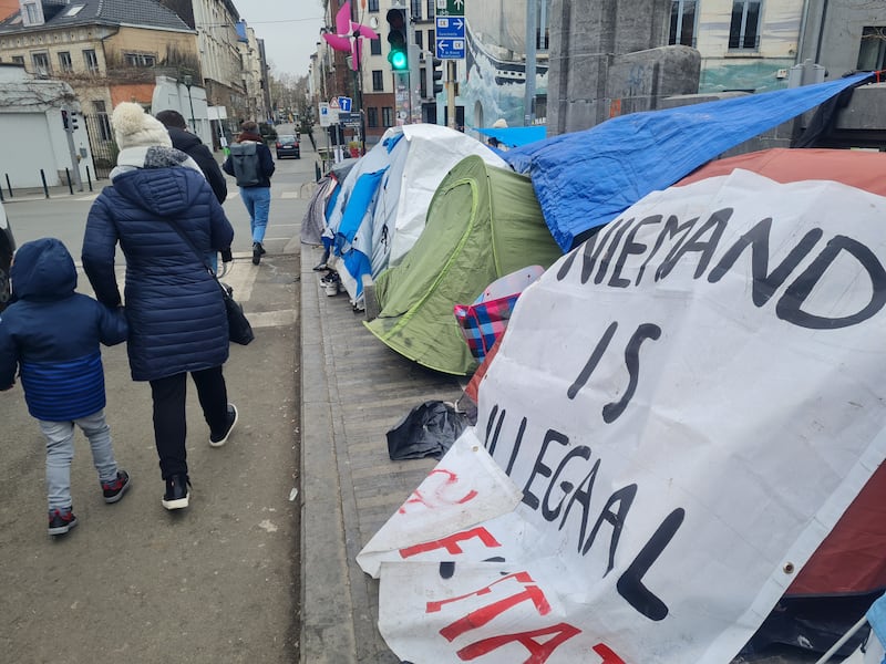 A local family walks by a tent  with a sign reading 'no one is illegal'. Photograph: Naomi O'Leary