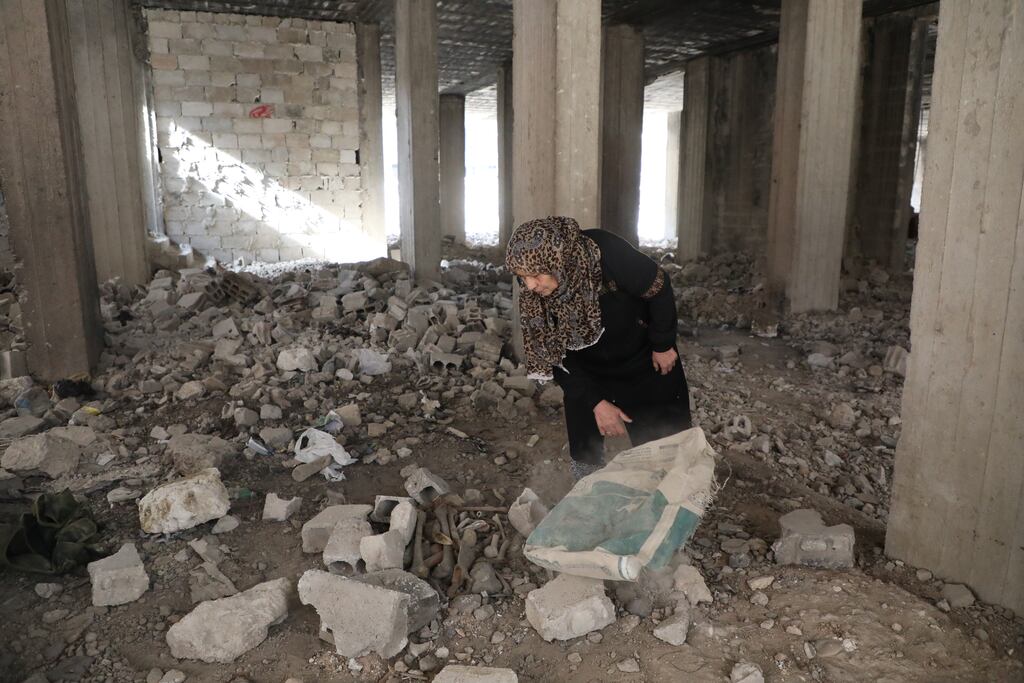 A woman overturns a bag near where bones lie on the ground of a ruined building on December 12th, in the Tadamon suburb of Damascus, Syria. Photograph: Ali Haj Suleiman/Getty