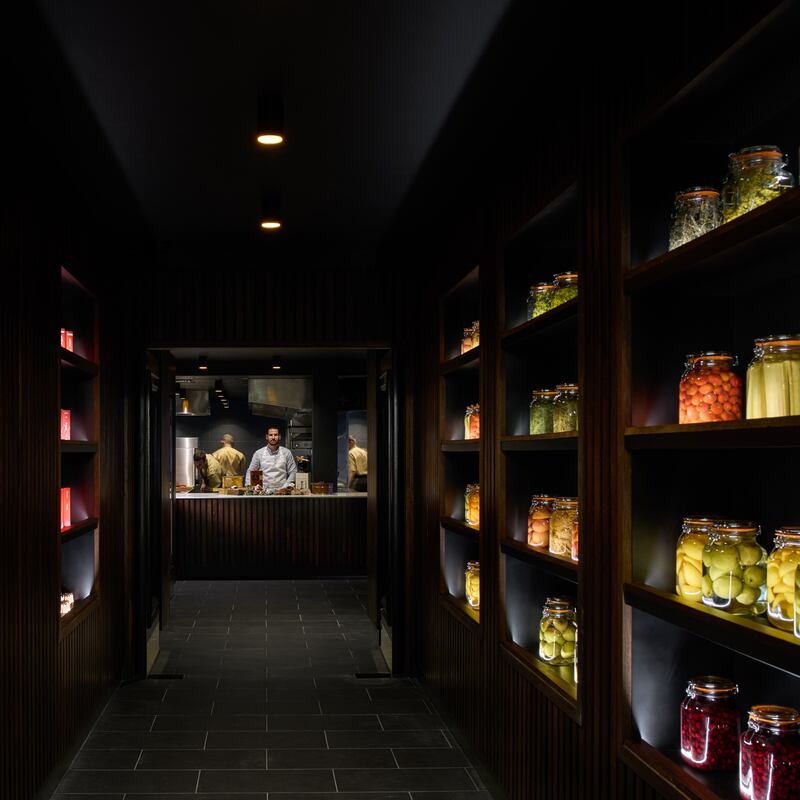 Vincent Crepel in his chef’s whites illuminated beneath one of the lights at the pass; the other chefs, dressed in khaki, blend into the dramatically dark background.